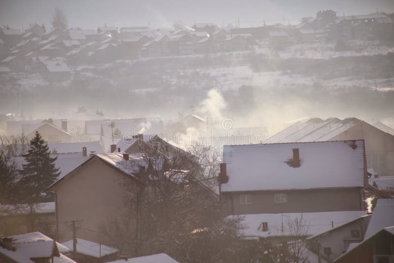 Rauchende Schlote an den Dächern mit Schnee von Häusern strahlen Rauch, Smog bei Sonnenaufgang, Schadstoffe eintragen Atmosphäre stockfotografie Rauchende Schlote an den Dächern mit Schnee von Häusern strahlen Rauch, Smog bei Sonnenaufgang, Schadstoffe eintragen Atmosphäre stockfotografie