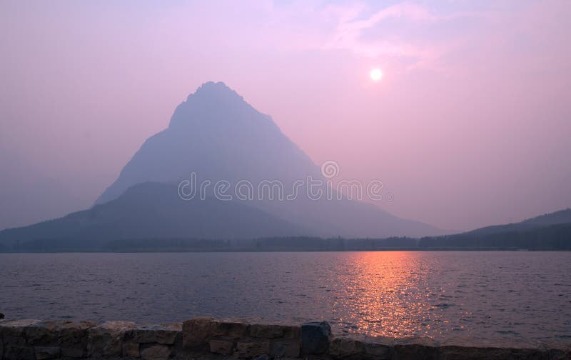 Rauchiger Sonnenuntergang über Swiftcurrent See vor Grinnell-Punkt im Glacier Nationalpark in Montana USA lizenzfreies stockbild Rauchiger Sonnenuntergang über Swiftcurrent See vor Grinnell-Punkt im Glacier Nationalpark in Montana USA lizenzfreies stockbild