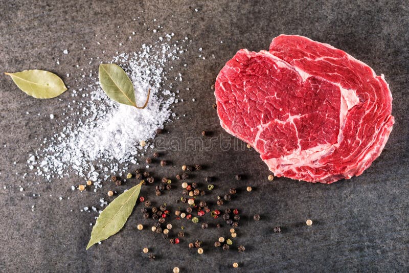 Raw beef steak fillet with ingredients like sea salt, pepper and bay leaves on black board, image for restaurant