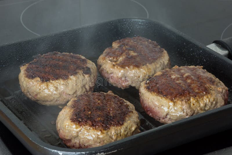 Raw Burgers, Beef in a Frying Pan on Cooking Surface in Kitchen Stock