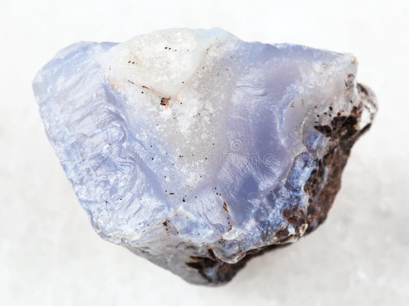 macro shooting of natural mineral rock specimen - raw crystal of blue Chalcedony gemstone on white marble background from Transbaikalia (Zabaykalye), Russia