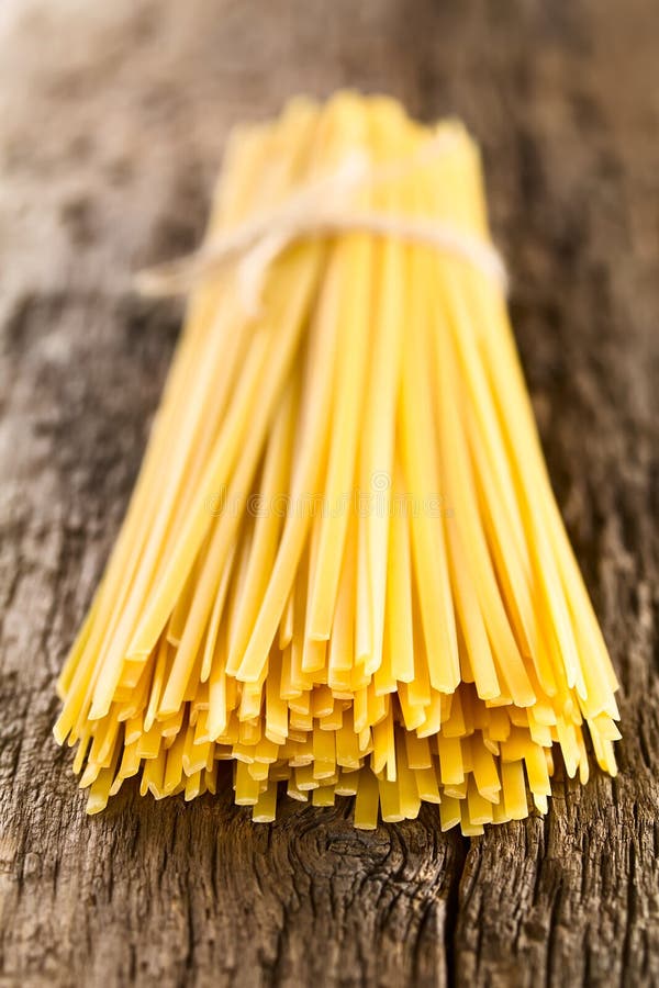 Raw flat long ribbon pasta called Fettuccini tied in a bundle on rustic wood Very Shallow Depth of Field, Focus on the front of the pasta strands. Raw flat long ribbon pasta called Fettuccini tied in a bundle on rustic wood Very Shallow Depth of Field, Focus on the front of the pasta strands