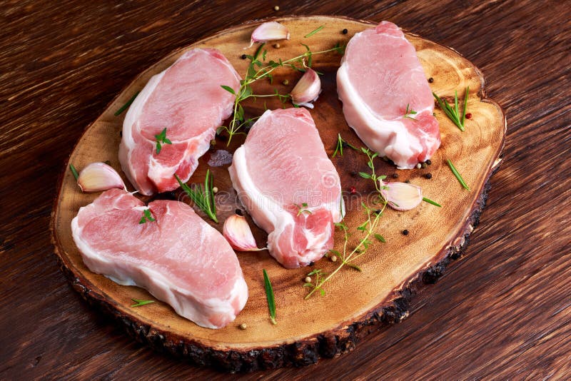 Raw Fresh Boneless Pork Chops with herbs. on wooden board.