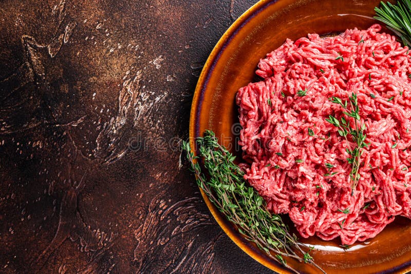 Raw Ground Beef or Veal Meat on a Rustic Plate with Herbs. Dark