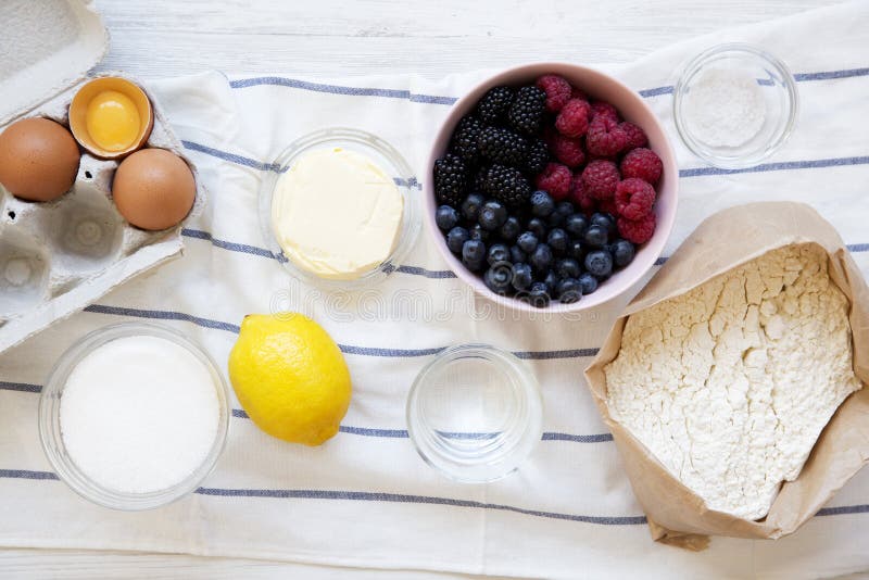 Raw ingredients: berries, flour, eggs, butter, lemon, water, sugar, salt for cooking berry pie on white wooden background, top vie