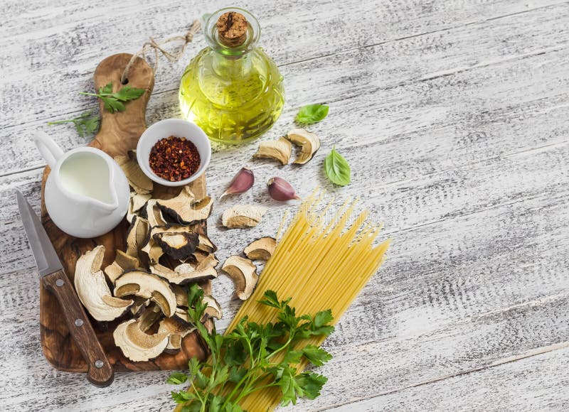 Raw ingredients for cooking pasta with porcini mushrooms - dried porcini mushrooms, spaghetti, cream, garlic, parsley, basil, oliv