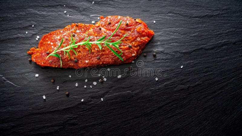 Raw marinated meat, beef steak on black slate background, top view