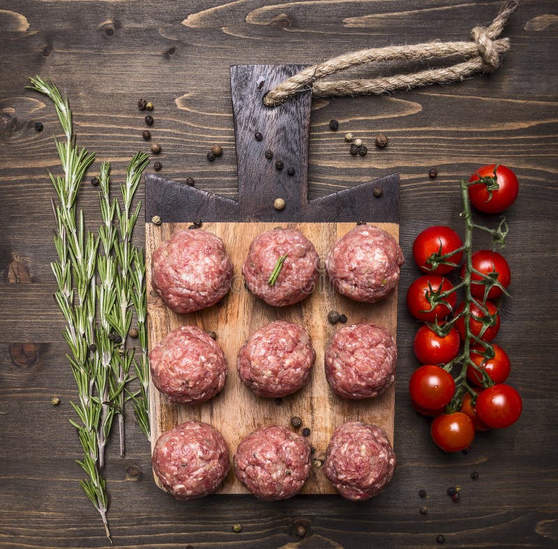 Raw meat balls with vegetables, butter and herbs on wooden rustic background top view close up