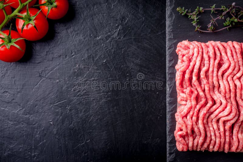 Raw minced meat on slate plate, ingredients for meat with tomato, chili pepper and herbson black background macro top view stock photo Raw minced meat on slate plate, ingredients for meat with tomato, chili pepper and herbson black background macro top view stock photo