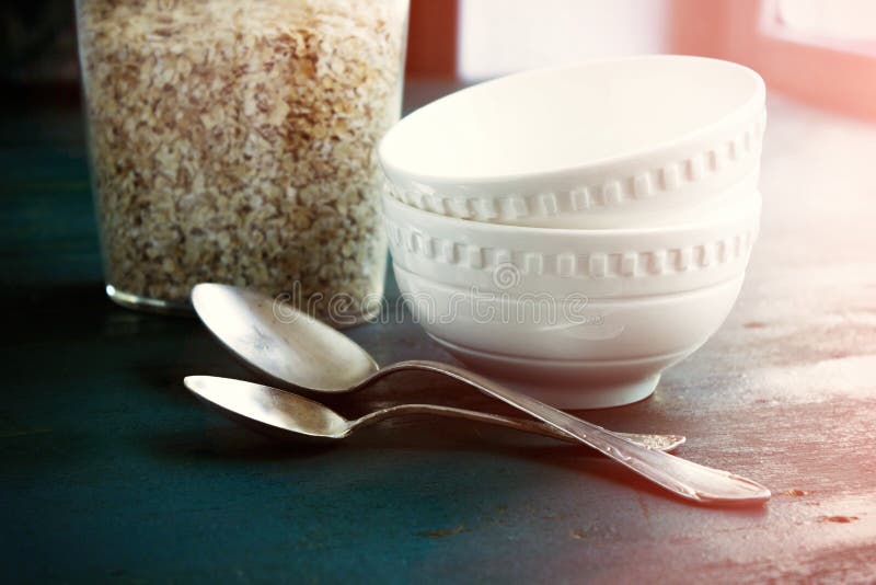 Raw oatmeal in a jar and a glass bowl on the table, spoons. Ingredients for Breakfast. TONED