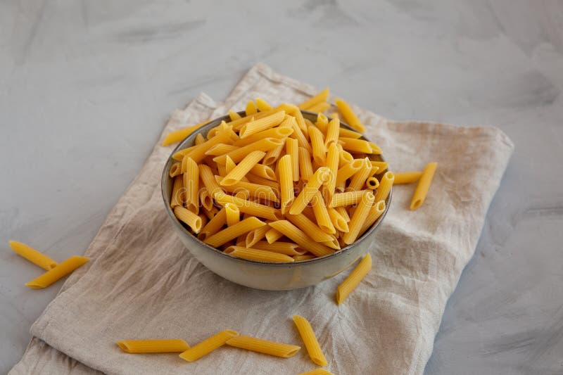 Raw Organic Penne Pasta in a Bowl on a Gray Background, Side View Stock