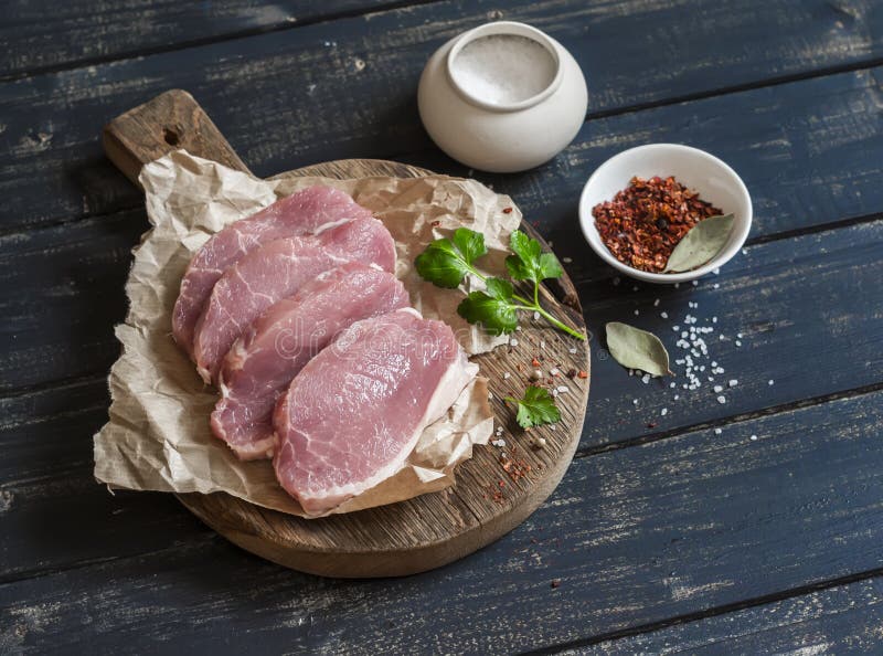 Raw pork chops and spices on a rustic wooden cutting board
