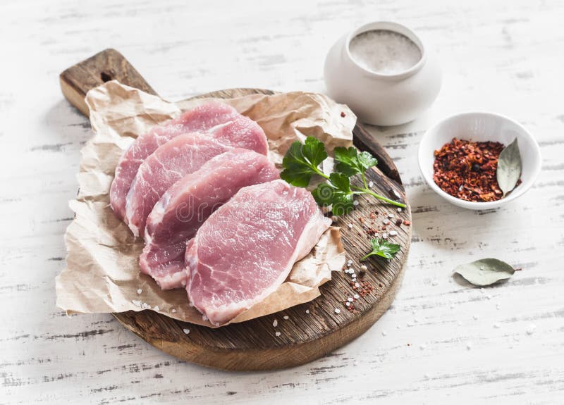 Raw pork chops and spices on a rustic wooden cutting board