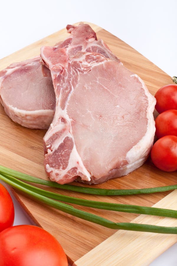 Raw pork chops with vegetables on chopping board