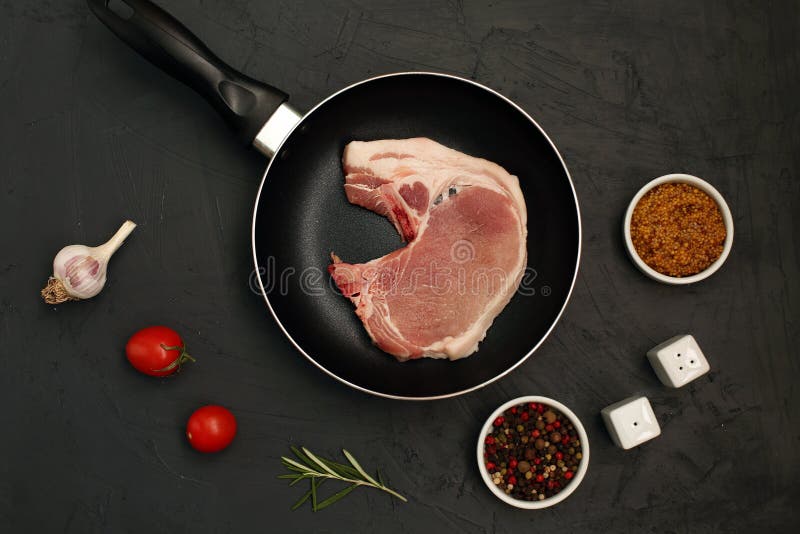 Raw pork loin chops in rustic skillet on black background