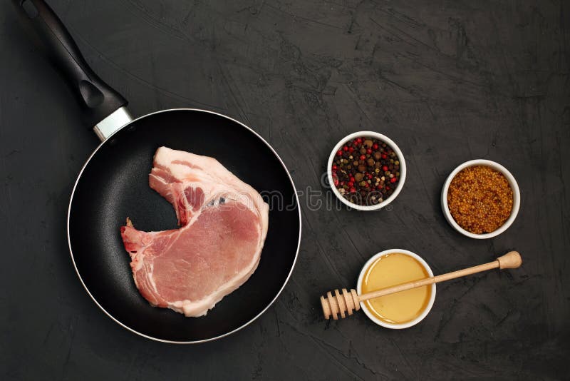 Raw pork loin chops in rustic skillet on black background