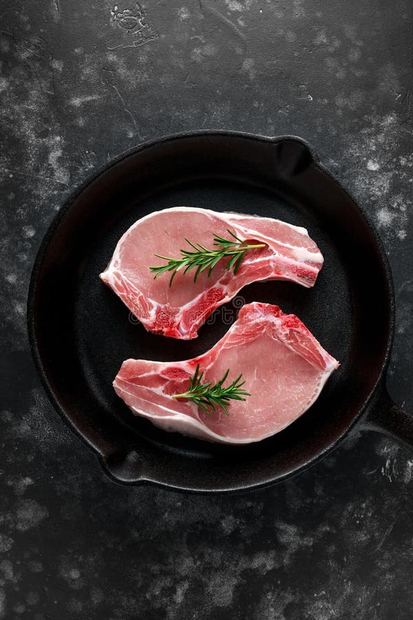 Raw Pork Loin chops in rustic skillet, pan with rosemary. top view. background