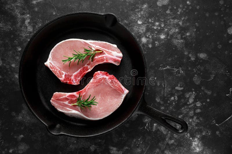 Raw Pork Loin chops in rustic skillet, pan with rosemary. top view. background