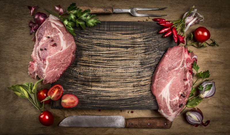 Raw pork meat chops with kitchen tools, fresh seasoning and ingredients for cooking on rustic wooden background, top view, frame.