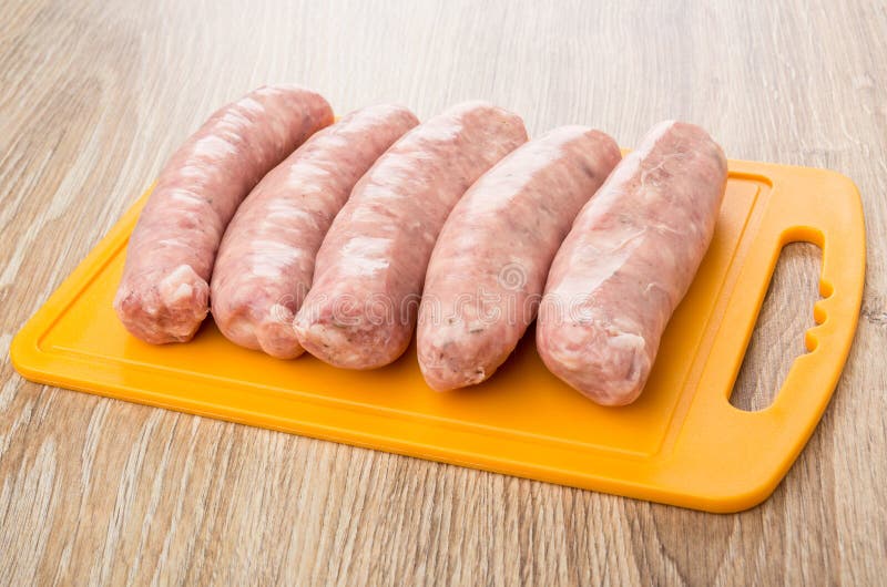 Raw Pork Sausages on Orange Plastic Cutting Board on Table Stock Photo