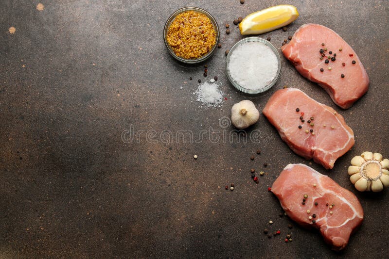 Raw pork steak, meat and ingredients for cooking, spices, herbs and vegetables on a dark background. top view. space for text