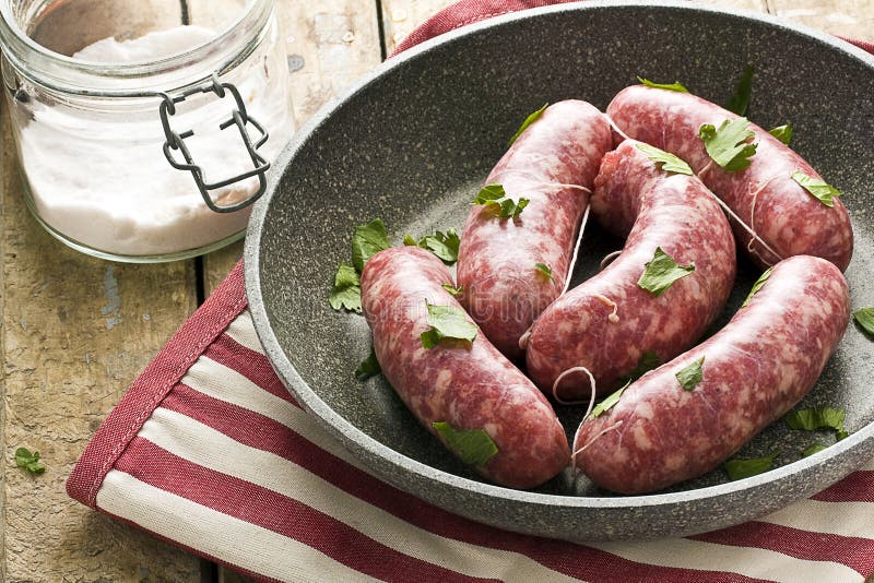 Crudo salchichas en negro sartén hierbas próximo sobre el sal sobre el rural de madera mesa.