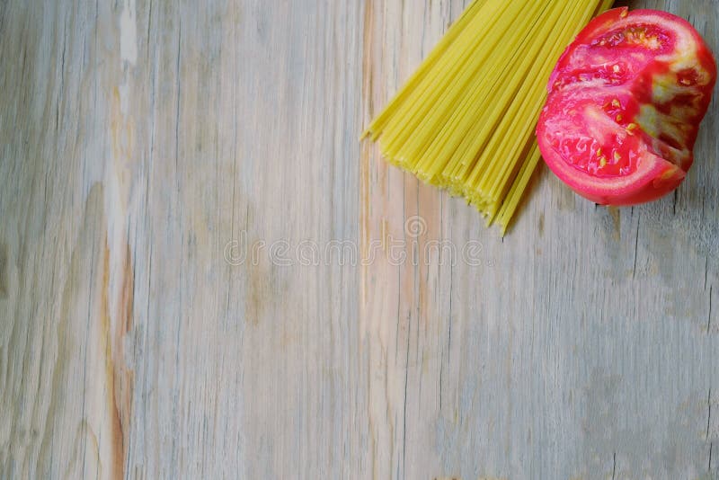 Raw Spaghetti Pasta and Half Tomato on Wood Background Stock Photo