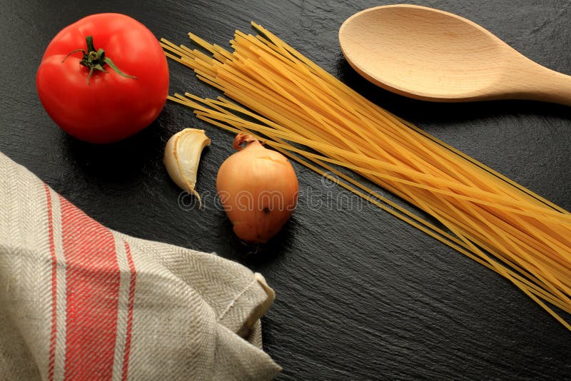 Raw spaghetti with tomato, garlic, onion, wooden trowel and kitchen towel royalty free stock photography Raw spaghetti with tomato, garlic, onion, wooden trowel and kitchen towel royalty free stock photography