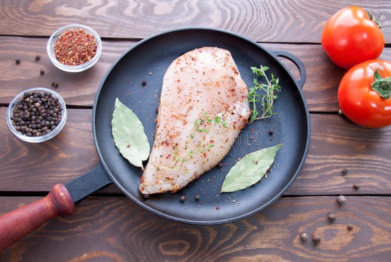 Raw steak from chicken fillet on an iron black frying pan with herbs and spices, laurel leaf and branches of thyme near stock image Raw steak from chicken fillet on an iron black frying pan with herbs and spices, laurel leaf and branches of thyme near stock image