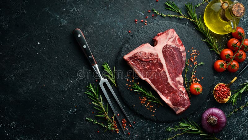 Raw T-bone steak on a stone table with thyme, rosemary and spices. Top view.