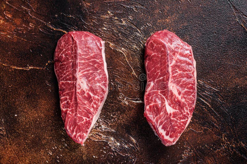 Raw Top Blade or Flat Iron Beef Meat Steaks on a Butcher Table. Dark