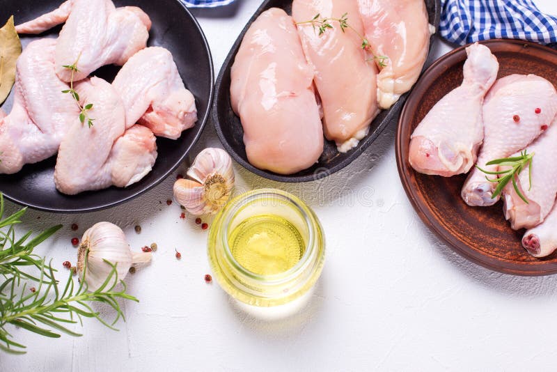 Raw uncooked chicken meat. Raw uncooked chicken legs or drumsticks, wings and breasts with ingredients for cooking on light textured background. Selective focus. View from above with copy space.