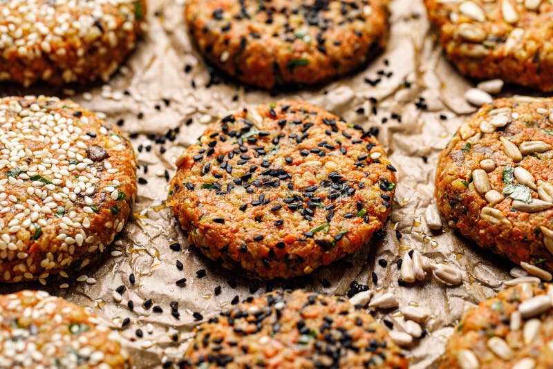 Raw vegan burgers made of carrots, millet, mix of seeds and herbs  on  parchment prepared for baking, close-up.