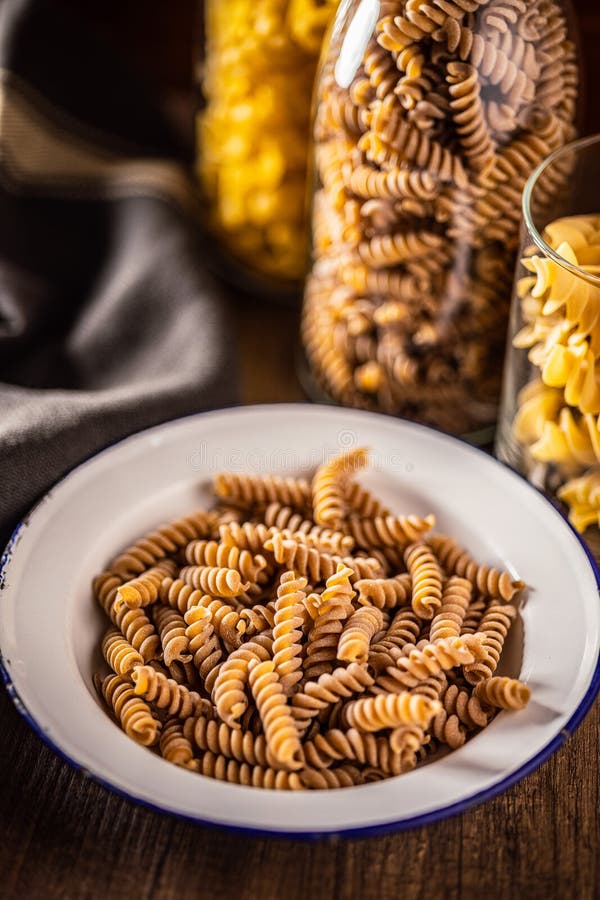 Raw whole grain fusilli pasta. Uncooked pasta on plate on wooden table stock photography