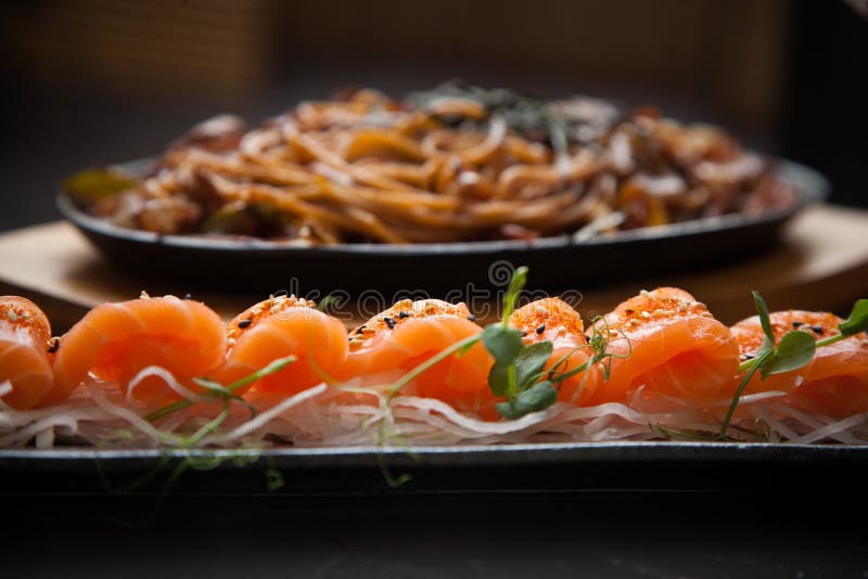 Raw полосы лосося суши на кровати и белой капусты запачканное yakisoba на фоне в тусклом свете стоковое изображение
