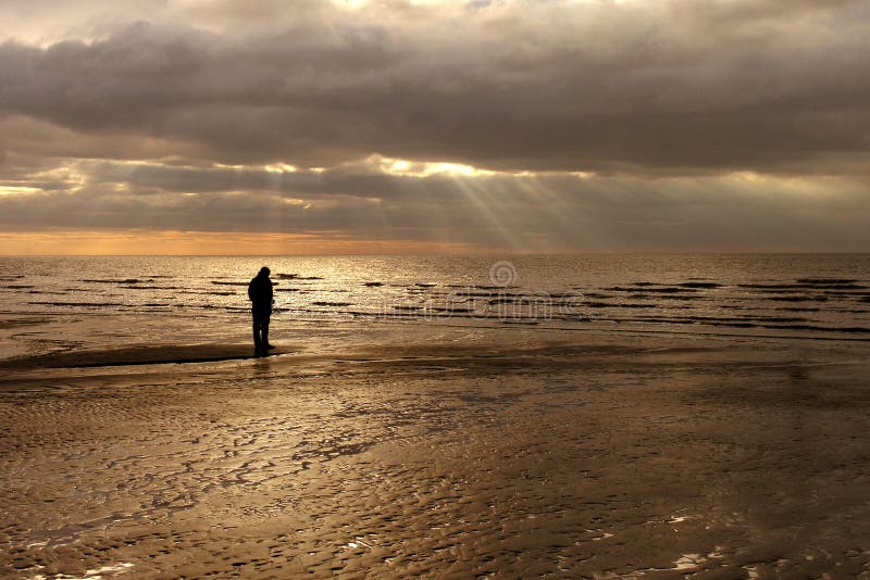 Person on beach against backdrop of receding sea and cloudy sunset sky. Person on beach against backdrop of receding sea and cloudy sunset sky