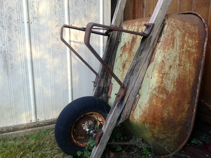 Rdzewiejący Wheelbarrow opiera na ogrodzeniu obrazy stock Rdzewiejący Wheelbarrow opiera na ogrodzeniu obrazy stock