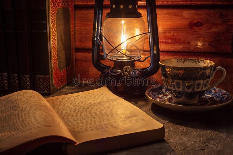 Reading a book in the light of an old hand-held kerosene lamp glows softly in a dark room on the table. Vintage style. stock photography Reading a book in the light of an old hand-held kerosene lamp glows softly in a dark room on the table. Vintage style. stock photography