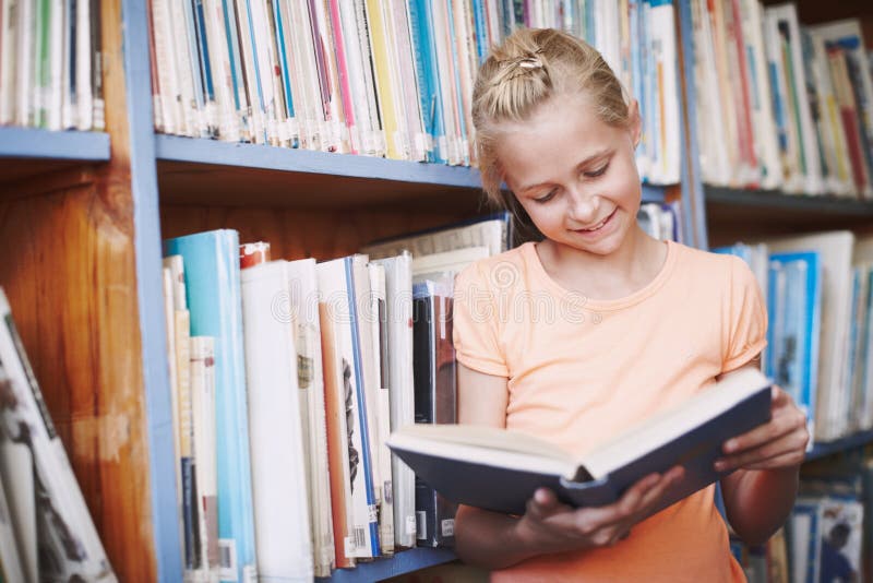 Reading opens up new worlds for her. A cute young girl reading a book in the library.