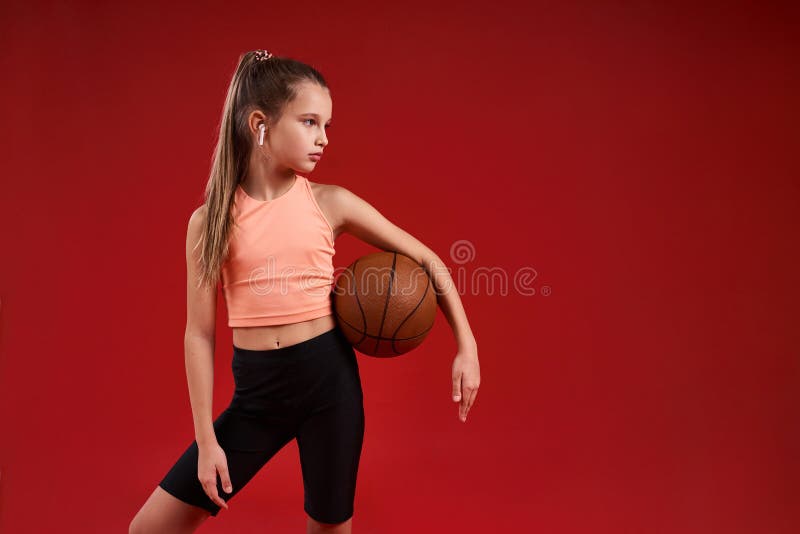 Ready for a game. A cute kid, girl is engaged in sport, she is looking aside while exercising with basketball. Isolated