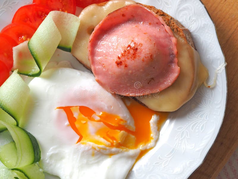 Ready-made Breakfast of eggs with liquid yolk, sausage and cheese sandwich decorated with tomatoes and cucumber