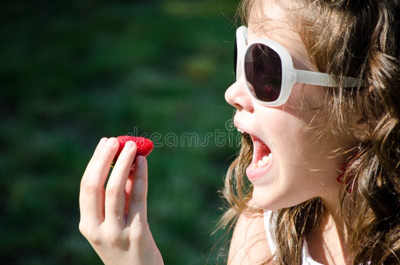 Young girl with sunglasses ready to eat a strawberry outdoor