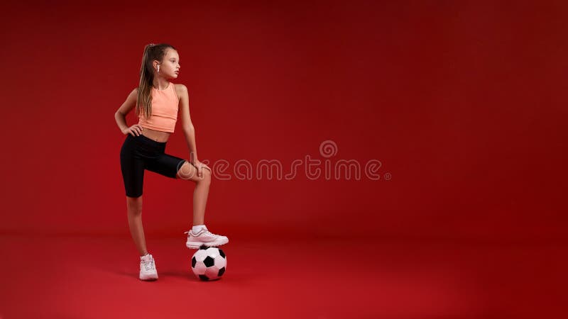 Ready to win. A cute kid, girl is engaged in sport, she is looking aside while exercising with football. Isolated on red