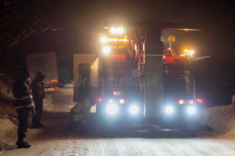 Dopravná nehoda kamiónu v noci na zasneženej zimnej ceste. Silne osvetlené Vrakovisko vyťahuje nákladné auto z visiaceho snehu.