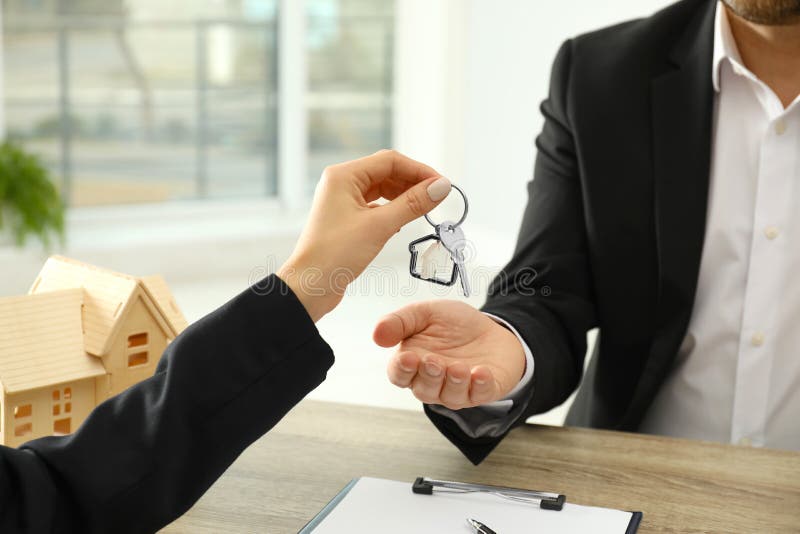Real Estate Agent Giving Key To Client at Table in Office Stock Image