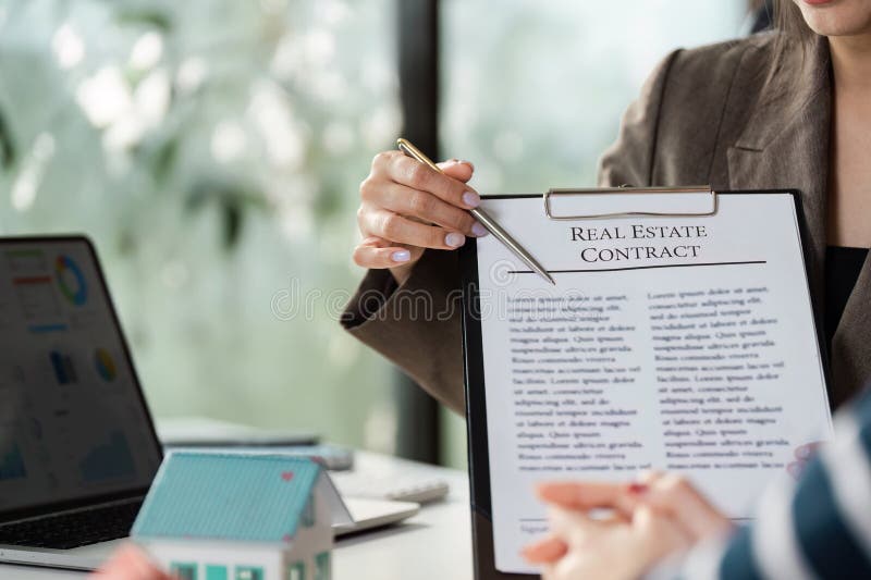 Real estate agent highlighting contract terms to client, showcasing model house and emphasizing agreement in office stock images