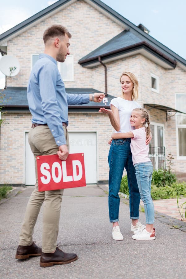 Real estate agent with sold sign giving key to young woman