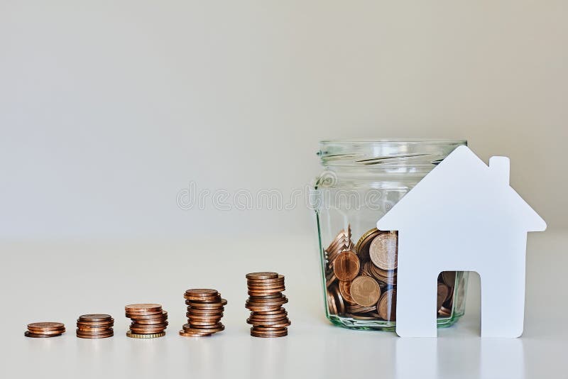 Real estate mortgage concept. Glass jar full of coins, stacks of coins and white paper house stock photos Real estate mortgage concept. Glass jar full of coins, stacks of coins and white paper house stock photos