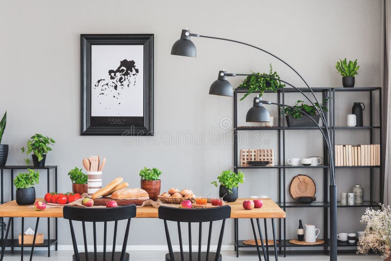 Real photo of an elegant daily room interior with a black shelf, lamp and dining table with herbs, bread and vegetables