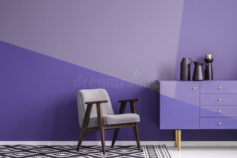 Real photo of a gray, wooden armchair on patterned, black and white rug in creative living room interior with geometric, violet w